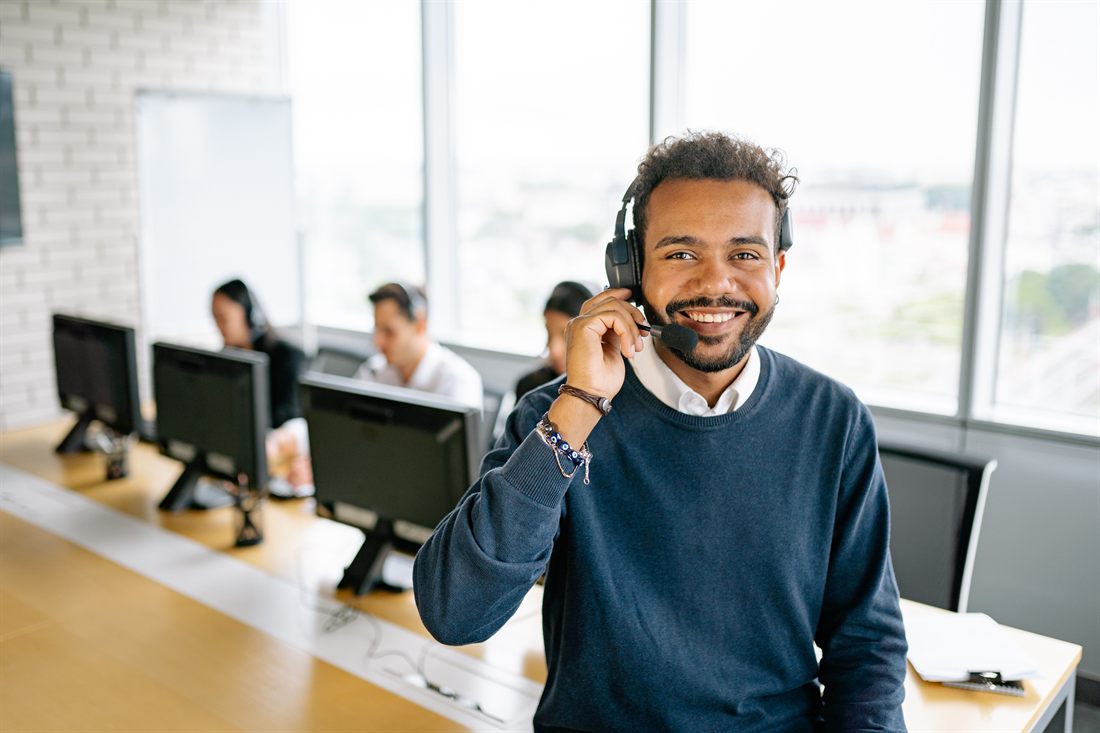 A smiling customer service adviser wearing a telephone headset at his desk.